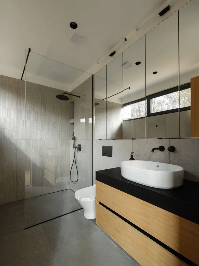 Light-filled bathroom of a Dwellii cabin: walk-in rain shower, oak vanity with black top, white basin, mirror wall