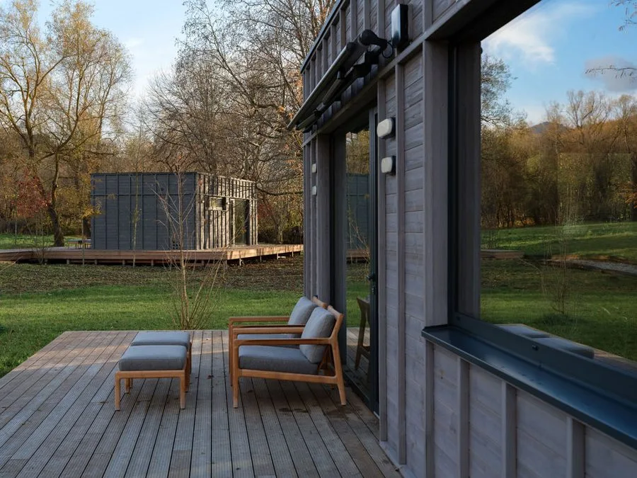 Timber deck with sun loungers of a Dwellii cabin, a second cabin beyond the meadow in golden evening light