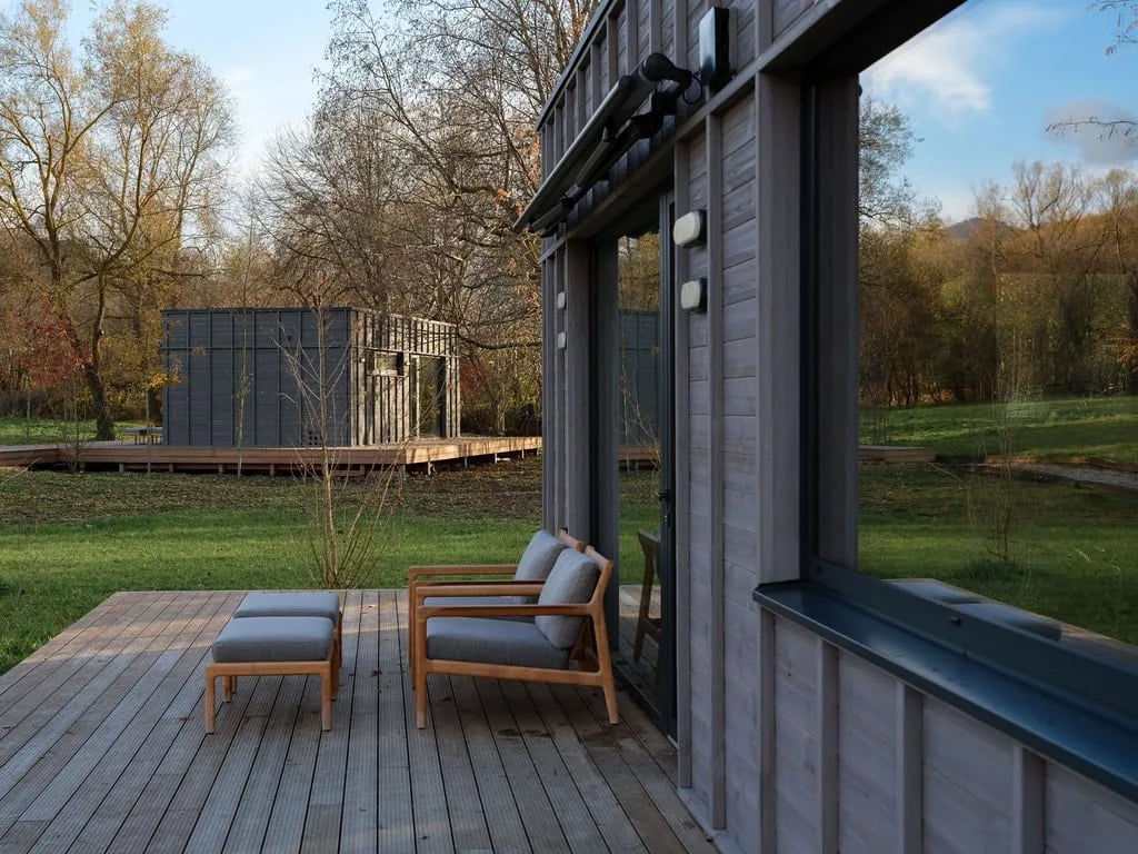 Holzdeck mit Liegestühlen einer Dwellii-Kabine, zweite Kabine jenseits der Wiese im goldenen Abendlicht