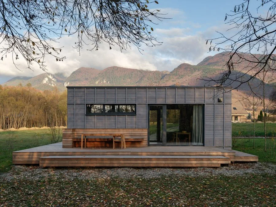 Grey Dwellii cabin with stepped deck and outdoor dining set against an autumnal mountain backdrop