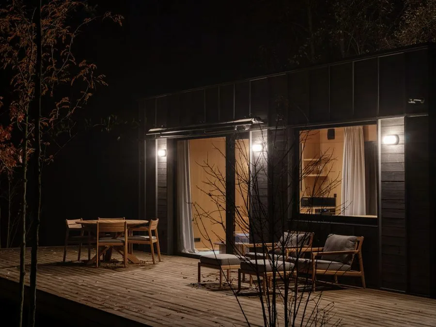 Dwellii cabin at night: warmly lit interior and illuminated terrace with dining set