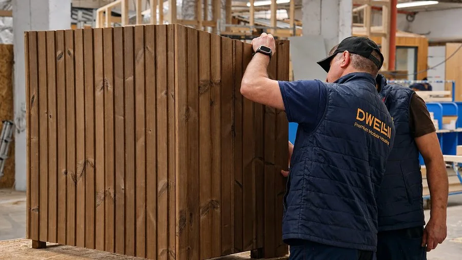 DWELLII factory worker inspecting a thermally modified timber façade module in the production hall