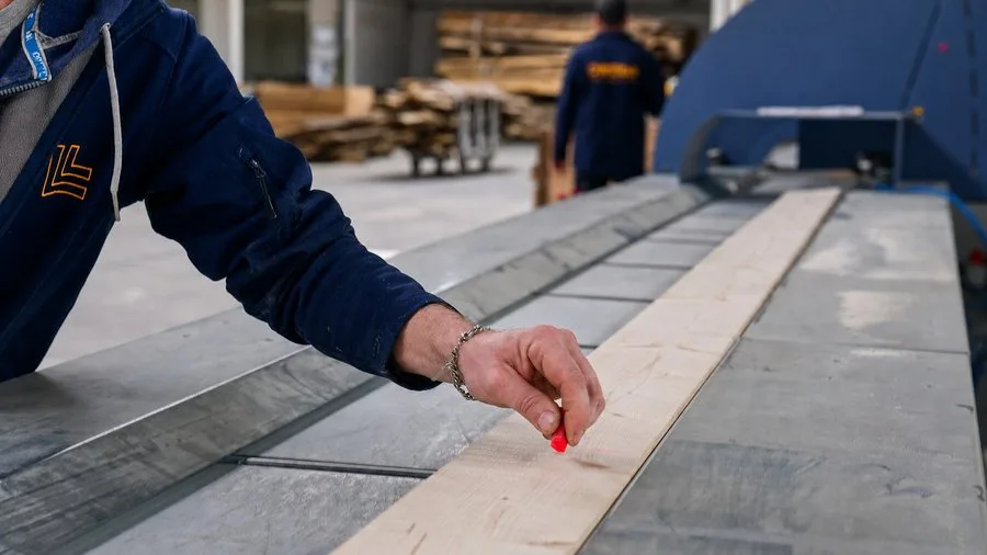 Hand of a factory worker marking a timber board at the red laser line in the DWELLII production hall