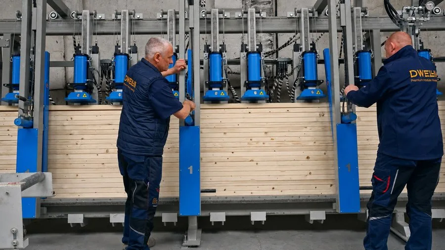 Two factory workers in DWELLII jackets operating the hydraulic press with pale timber slats