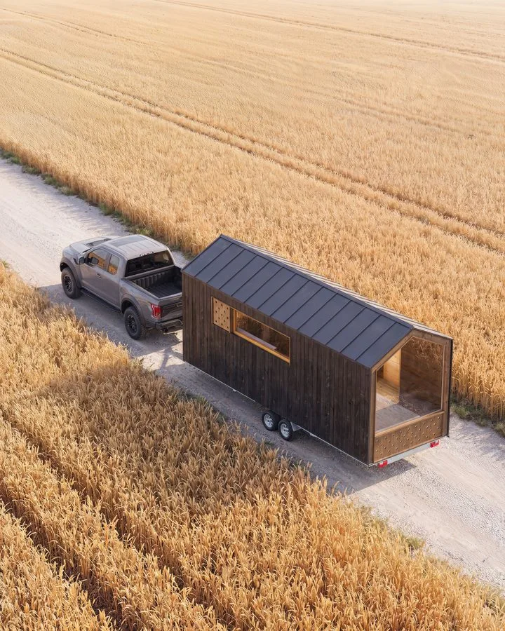 Render of the THOW 2 from above: pick-up truck towing the tiny house along a track through a golden wheat field