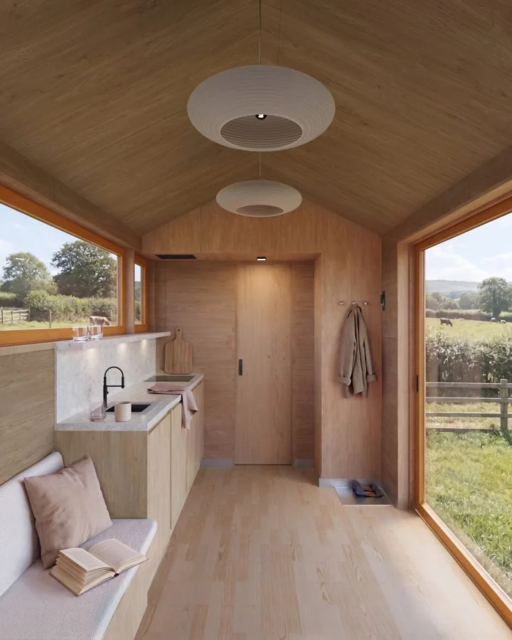 Render of the THOW 2 interior: living room under a gable roof with timber surfaces, kitchen unit and glazing to the meadow
