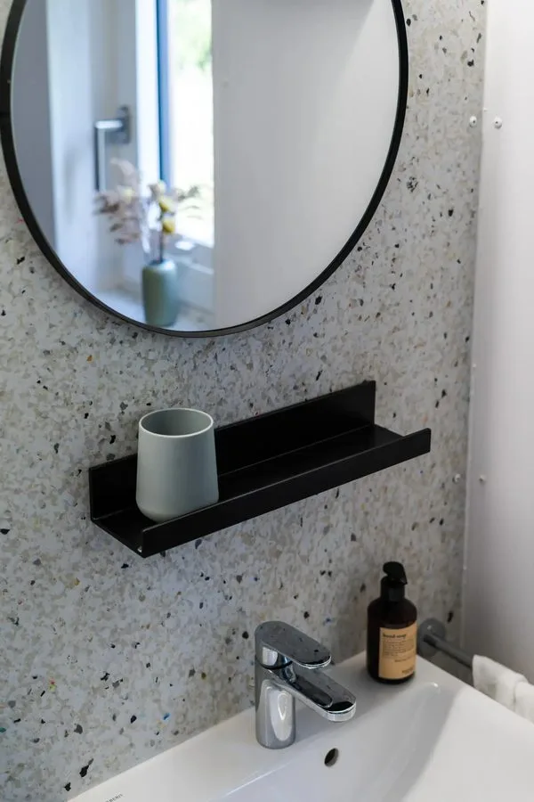 Bathroom of the Tinca Cabin in detail: white basin, round black mirror, terrazzo-effect wall, black shelf