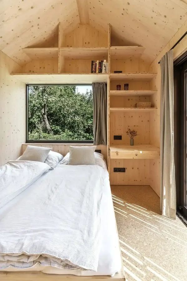 Bedroom of the Tinca Cabin: white bed linen, visible timber ceiling in the gable, ladder shelf and window to the green