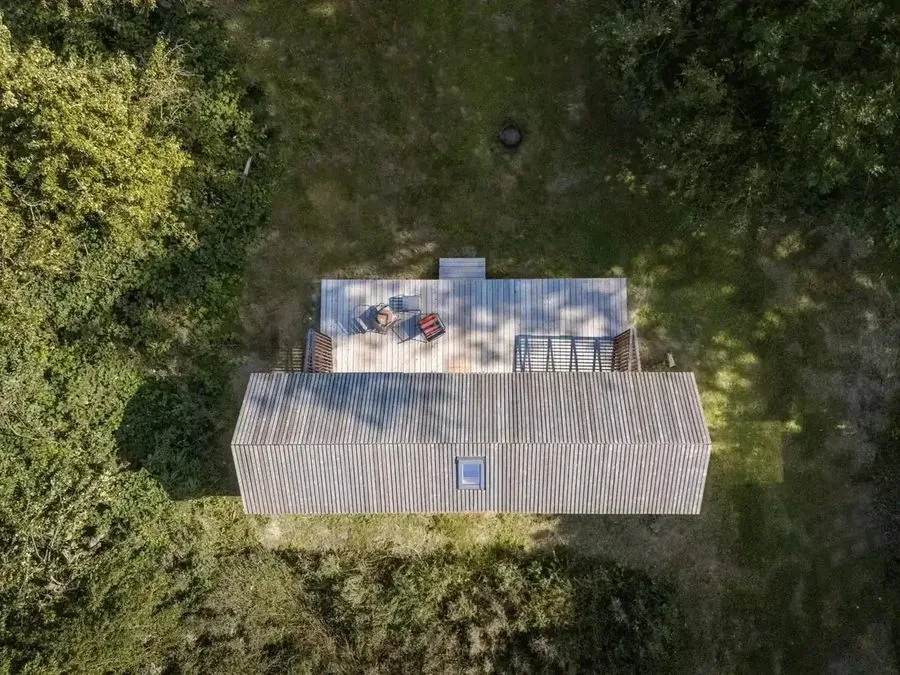 Aerial view of the Tinca Cabin from above: roof and terrace area among trees and meadow