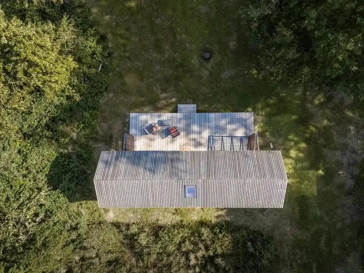 Luftaufnahme der Tinca Cabin von oben: Dach und Terrassenfläche zwischen Bäumen und Wiese