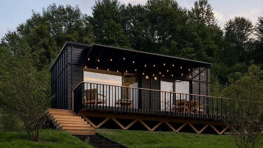 The TR01 from outside: dark timber façade, wrap-around terrace with railing, set in greenery