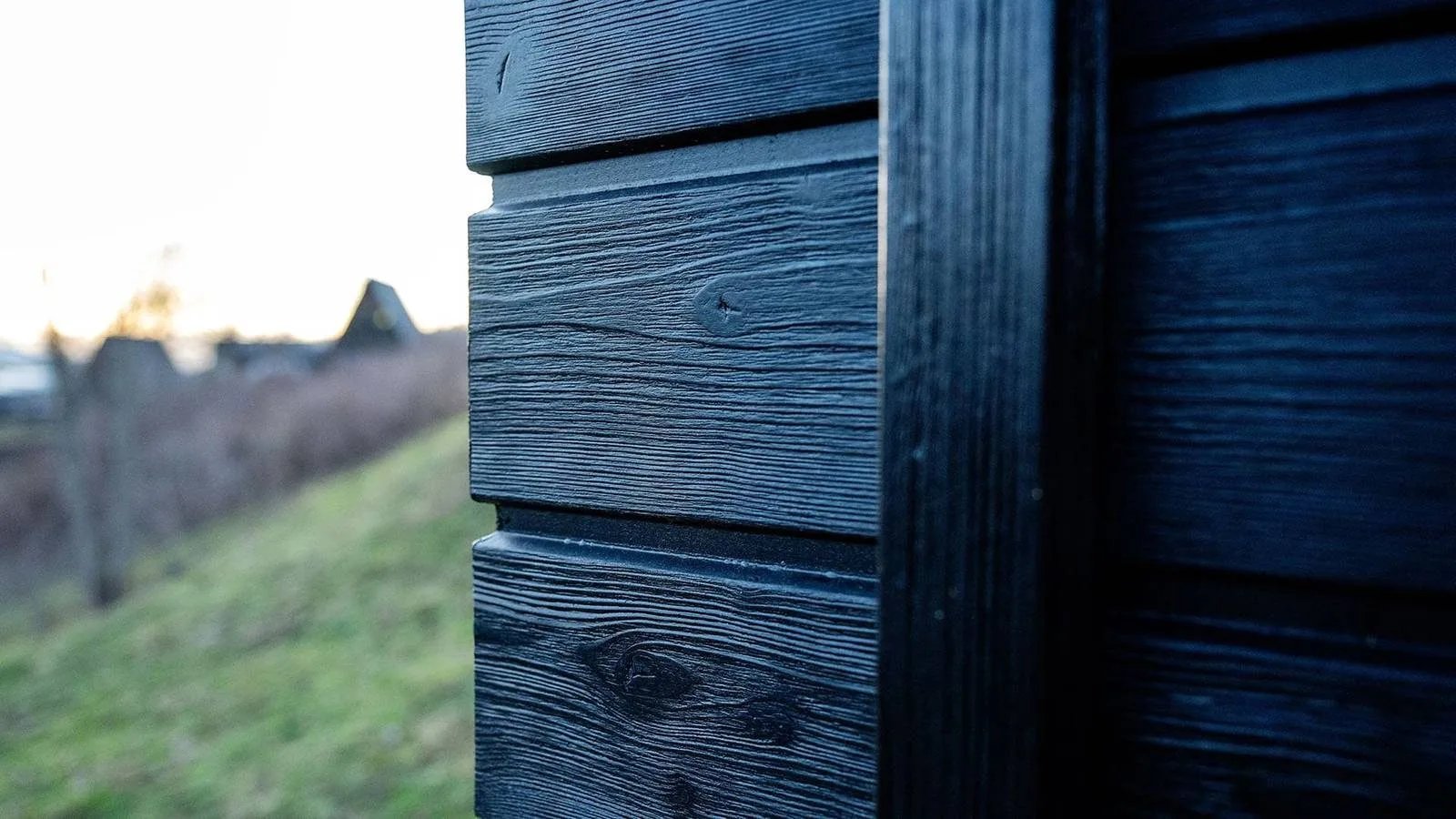 Detail der dunklen Holzfassade des TR01 in der Abendsonne, Wiese im Hintergrund