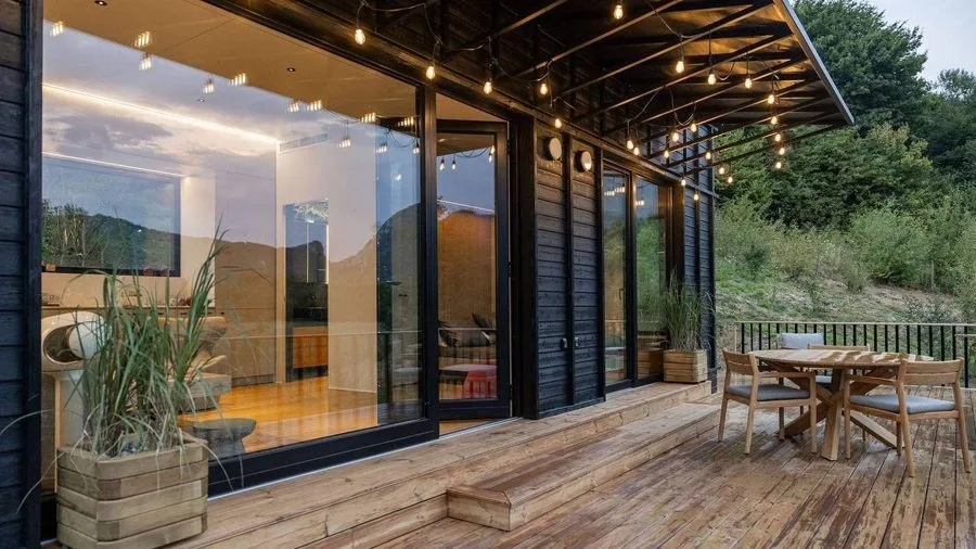 Terrace of the TR01 running along the glazed front: timber dining set, fairy lights under the canopy