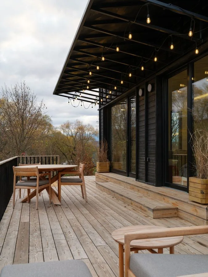 Terrace of the TR01 in portrait: fairy lights under the black canopy, round dining table, view into the valley