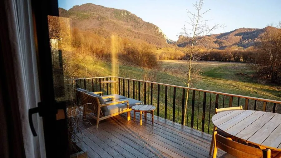 Evening mood on the TR01 terrace: sun lounger and table in front of the glass front, mountain meadow in last light