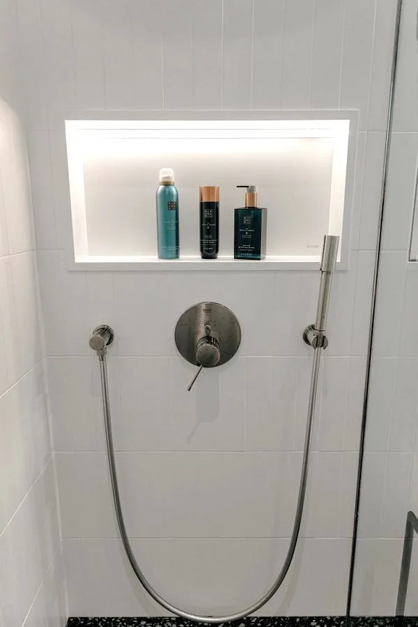 Bathroom in the TR3M showhouse: frameless walk-in shower without threshold, white basin on oak cabinet, terrazzo floor and rolled towel at the basin