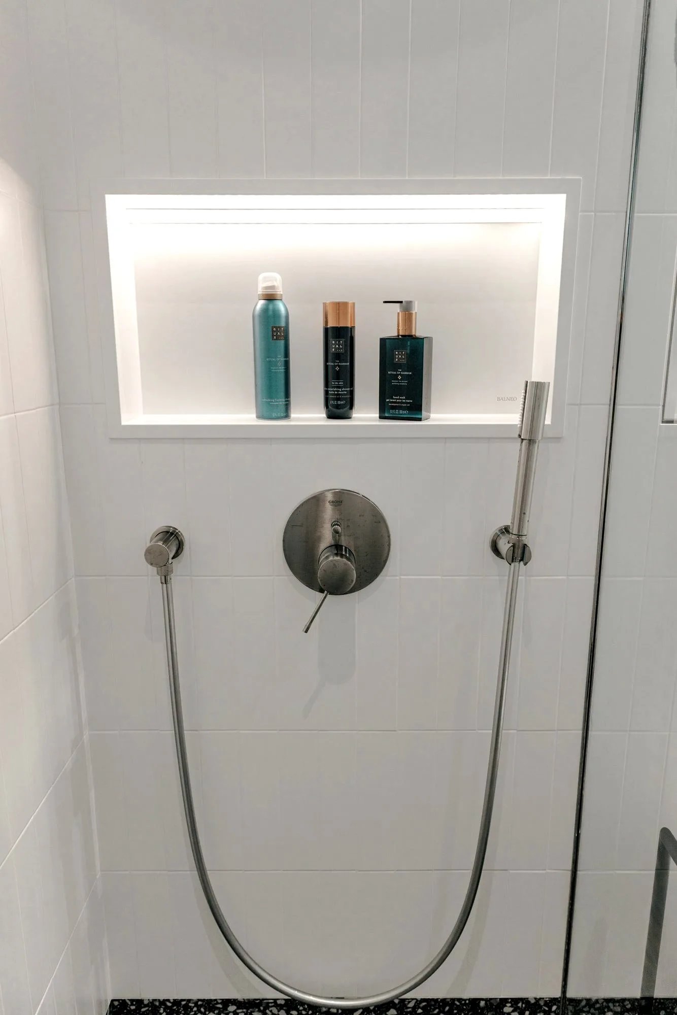 Badezimmer im Musterhaus TR3M: begehbare Glasdusche ohne Schwelle, weißes Waschbecken auf Eichenunterschrank, Terrazzoboden und gerolltes Handtuch am Waschbecken