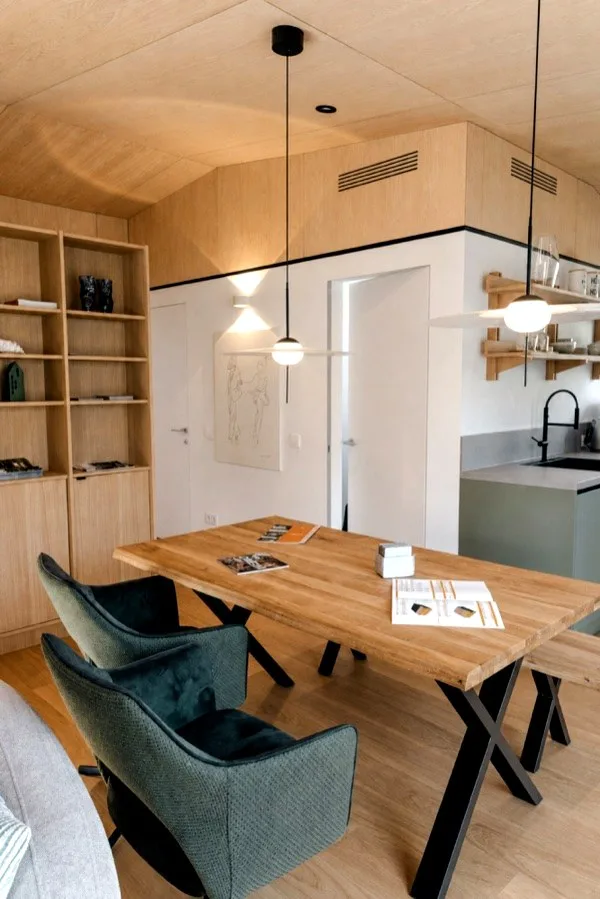 Dining area in the TR3M showhouse: oak table, green upholstered chairs, pendant light, kitchen directly behind