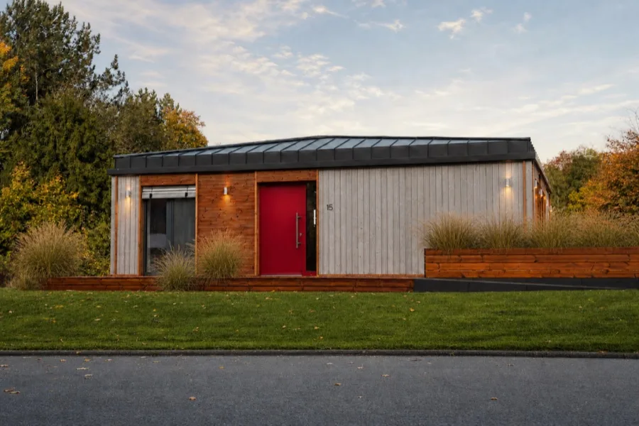 Street façade of the TR3M showhouse with dark red front door, planted wall and autumn leaves on the lawn