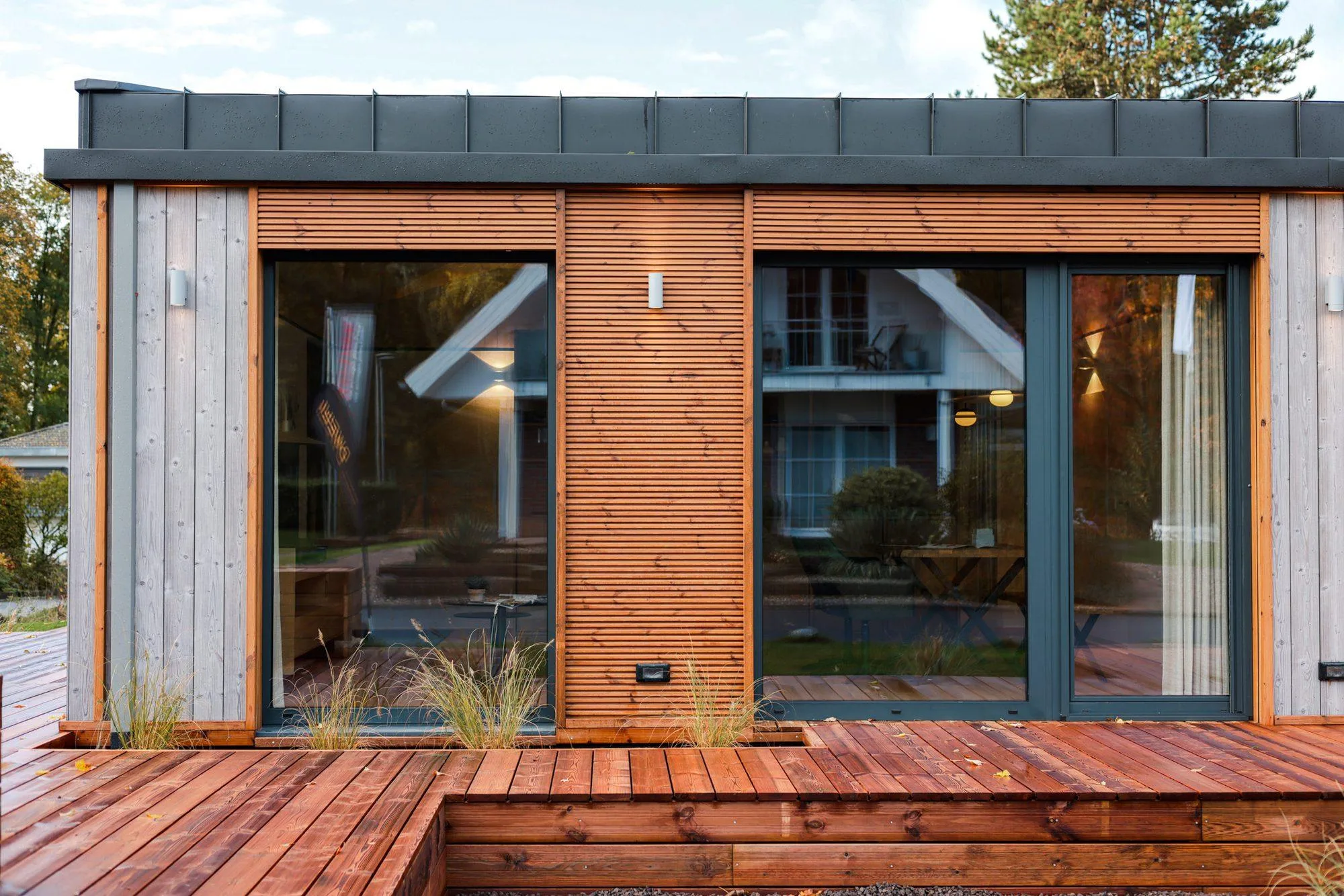 Terrace side of the TR3M showhouse: large sliding glazing, warm timber and grey larch cladding, stepped deck