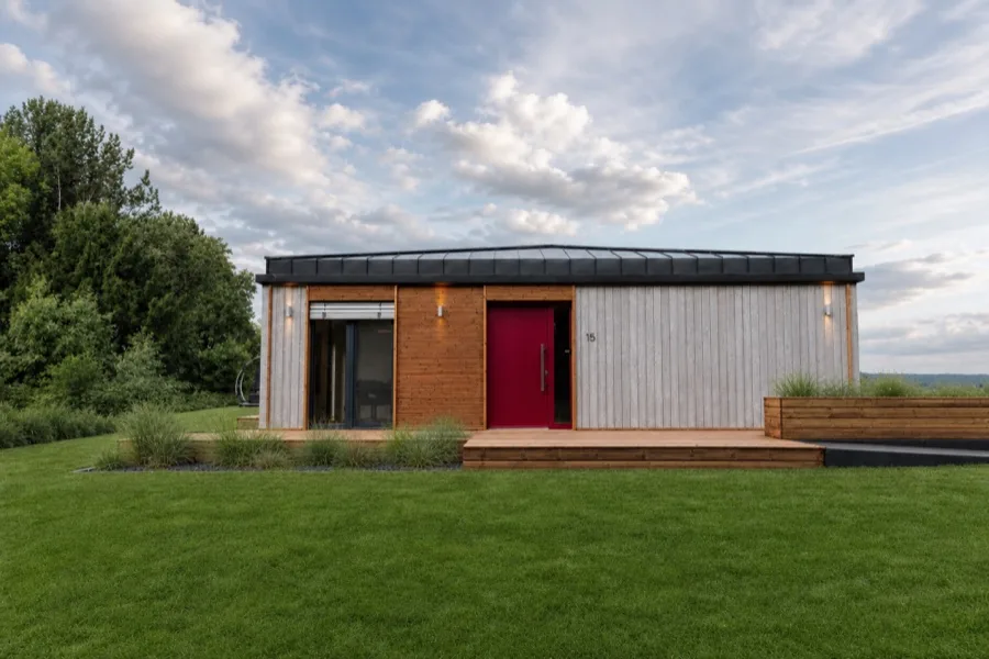 Garden façade of the TR3M showhouse across a wide lawn, red front door, large sky with clouds