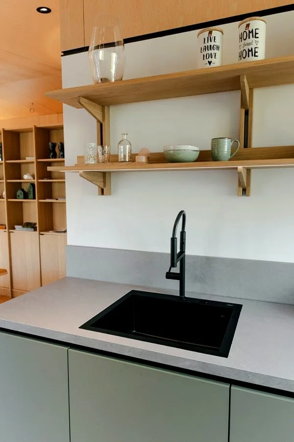 Detail of the kitchen in the TR3M showhouse: black sink with tap, stone worktop and oak shelves