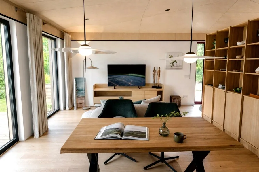 Blick vom Esstisch durch den Wohnraum des TR3M-Musterhauses — Kaffee auf dem Tisch, dahinter Sofa und Gartenblick